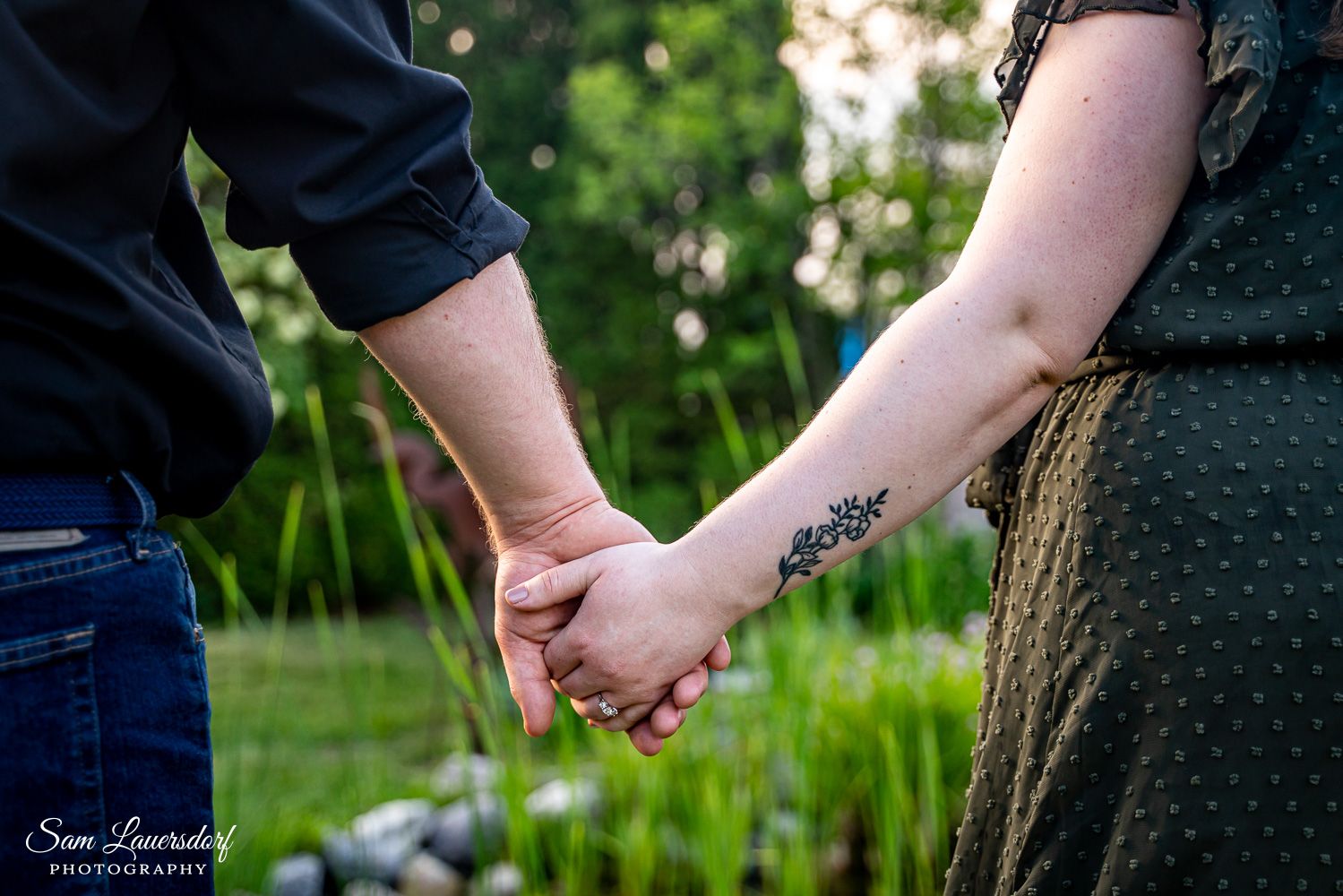 Close up shot of a couple holding hands with a small tattoo visible on one arm.