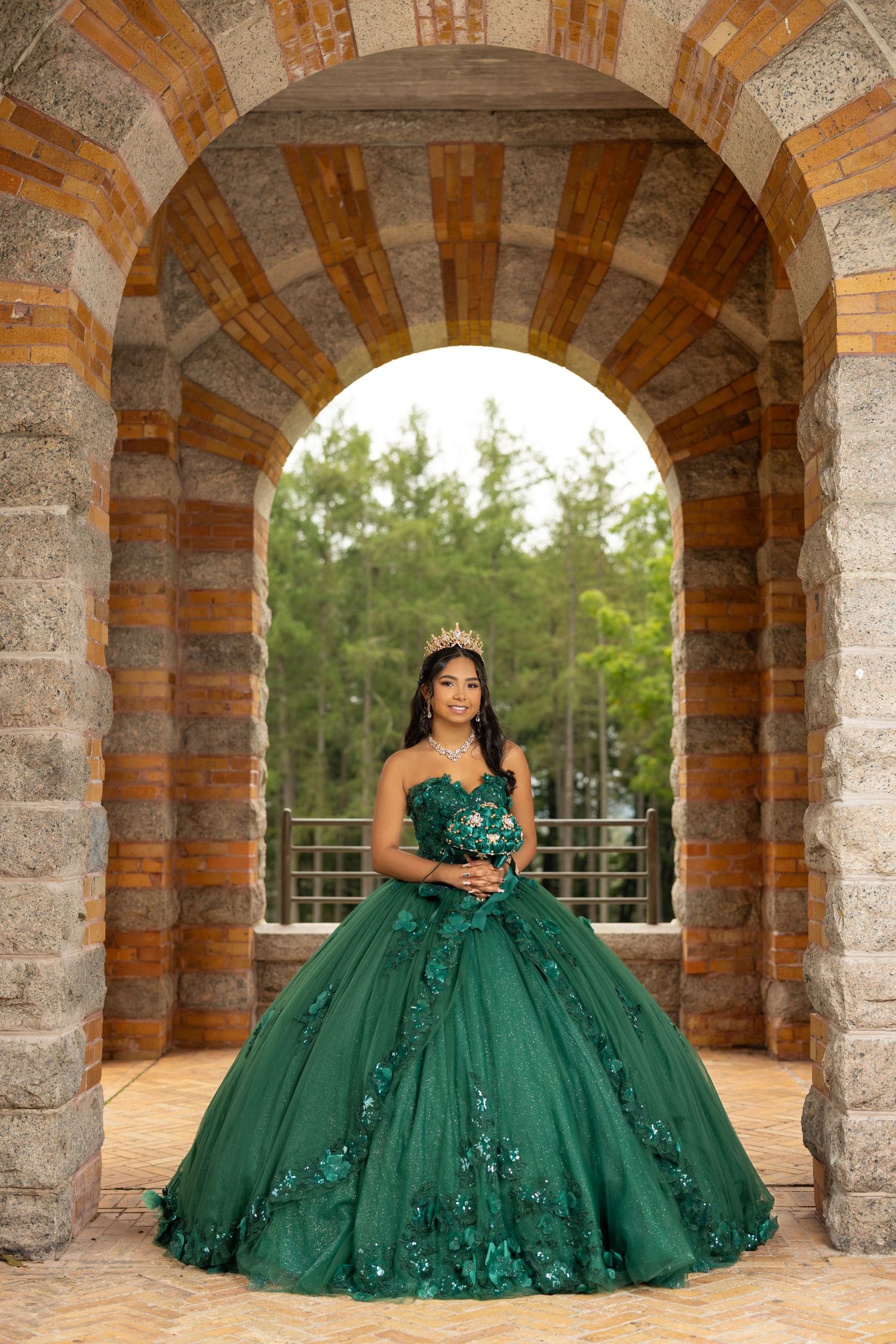 Emerald green ball gown with floral details photographed under stone archway.