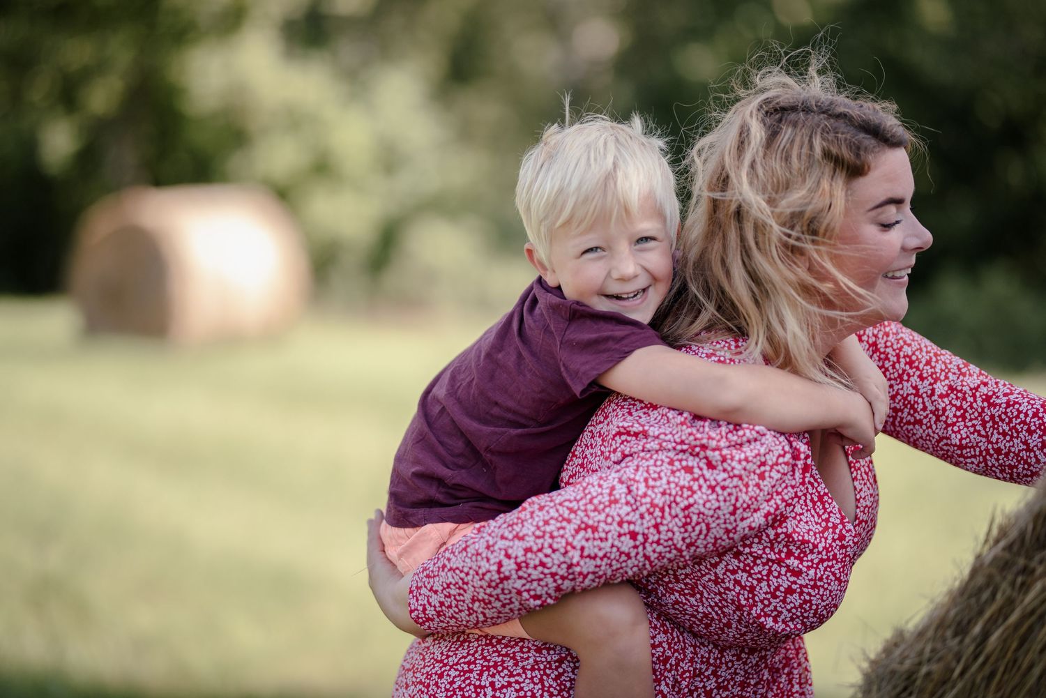 A playful piggyback ride moment outdoors in a floral print dress and purple shirt.