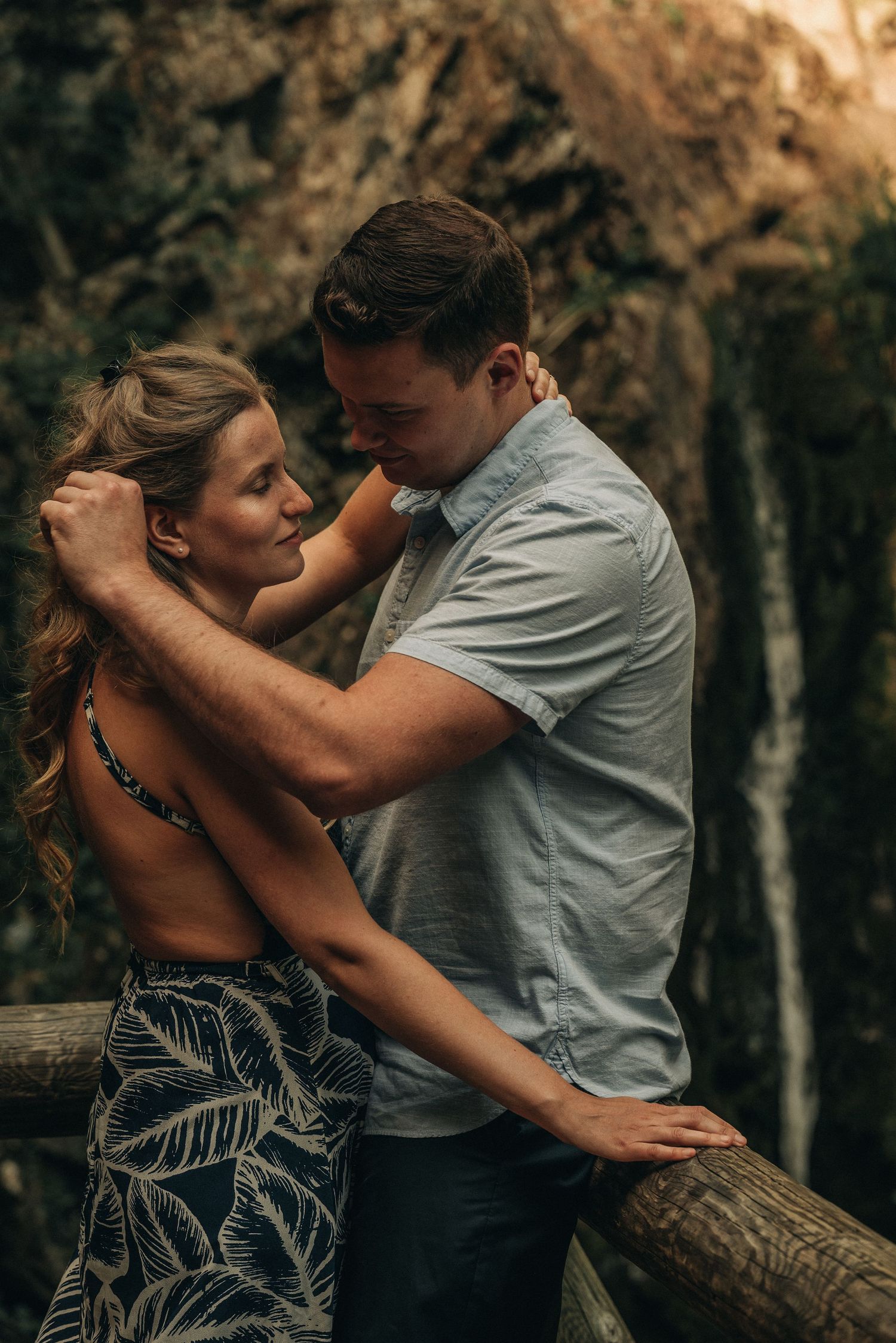 An intimate embrace captured in warm lighting against a natural forest backdrop.