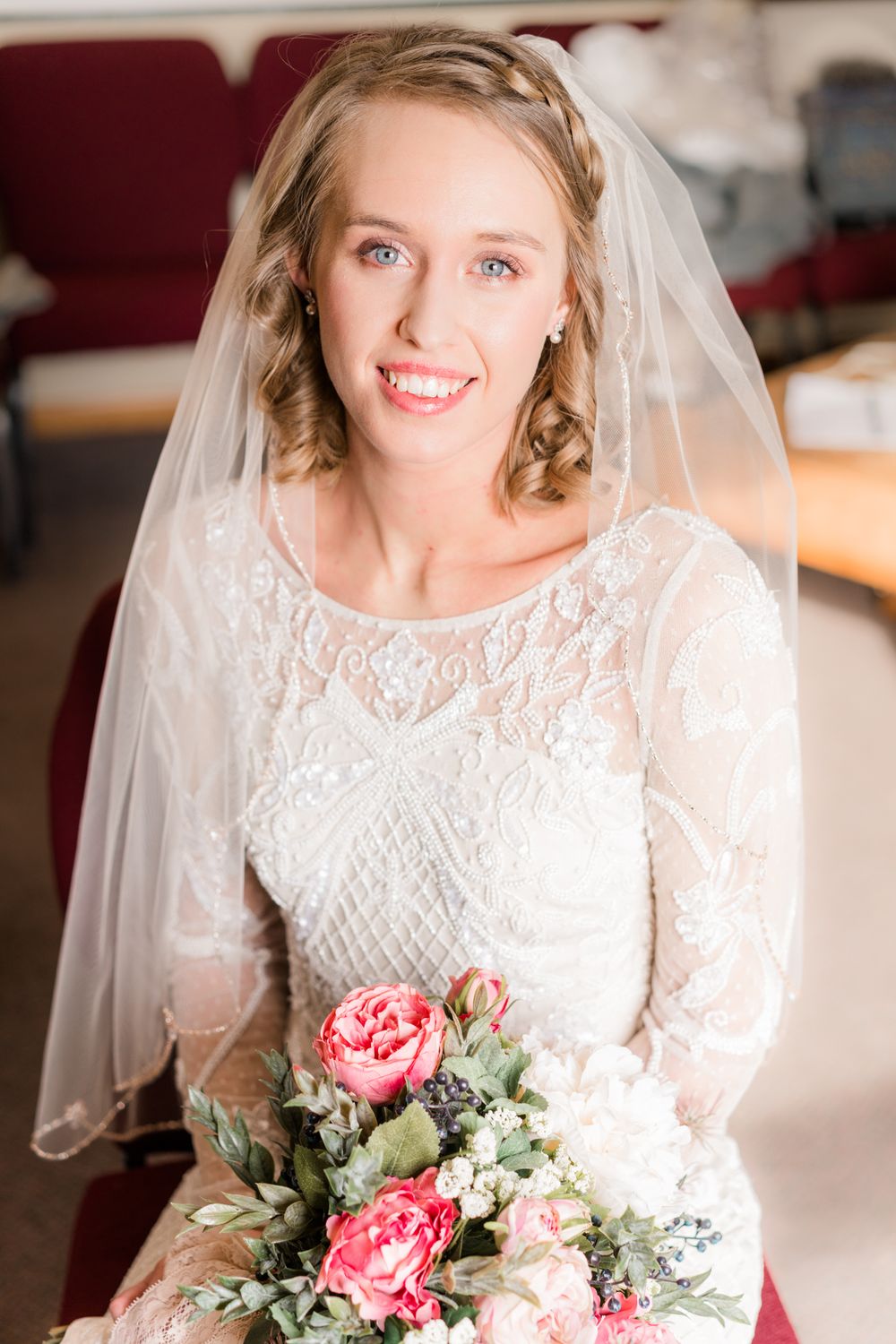 A bride wearing a delicate lace gown and veil holds a pink floral bouquet.