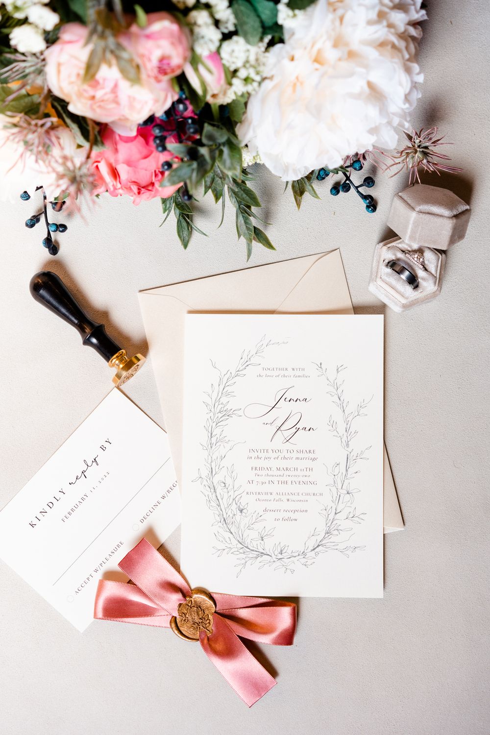 Elegant wedding invitation with pink floral details, wax seal, and calligraphy against a light background.