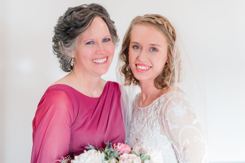 Bride in lace dress and companion in burgundy dress pose with floral bouquets.
