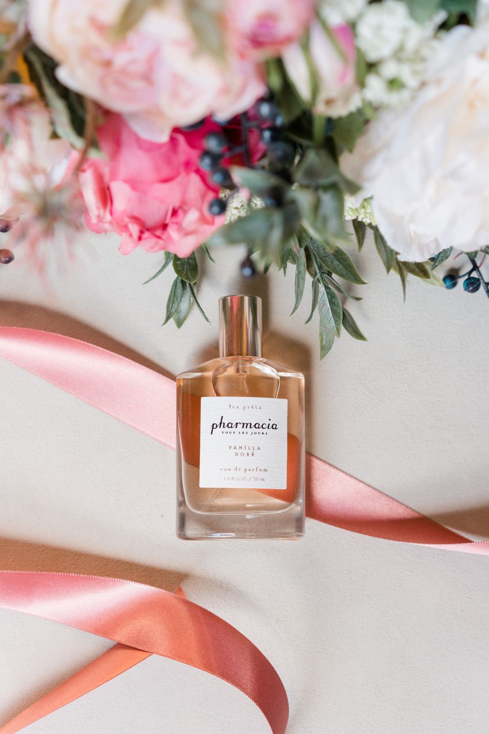 Perfume bottle with pink ribbon and floral arrangements on a light surface.