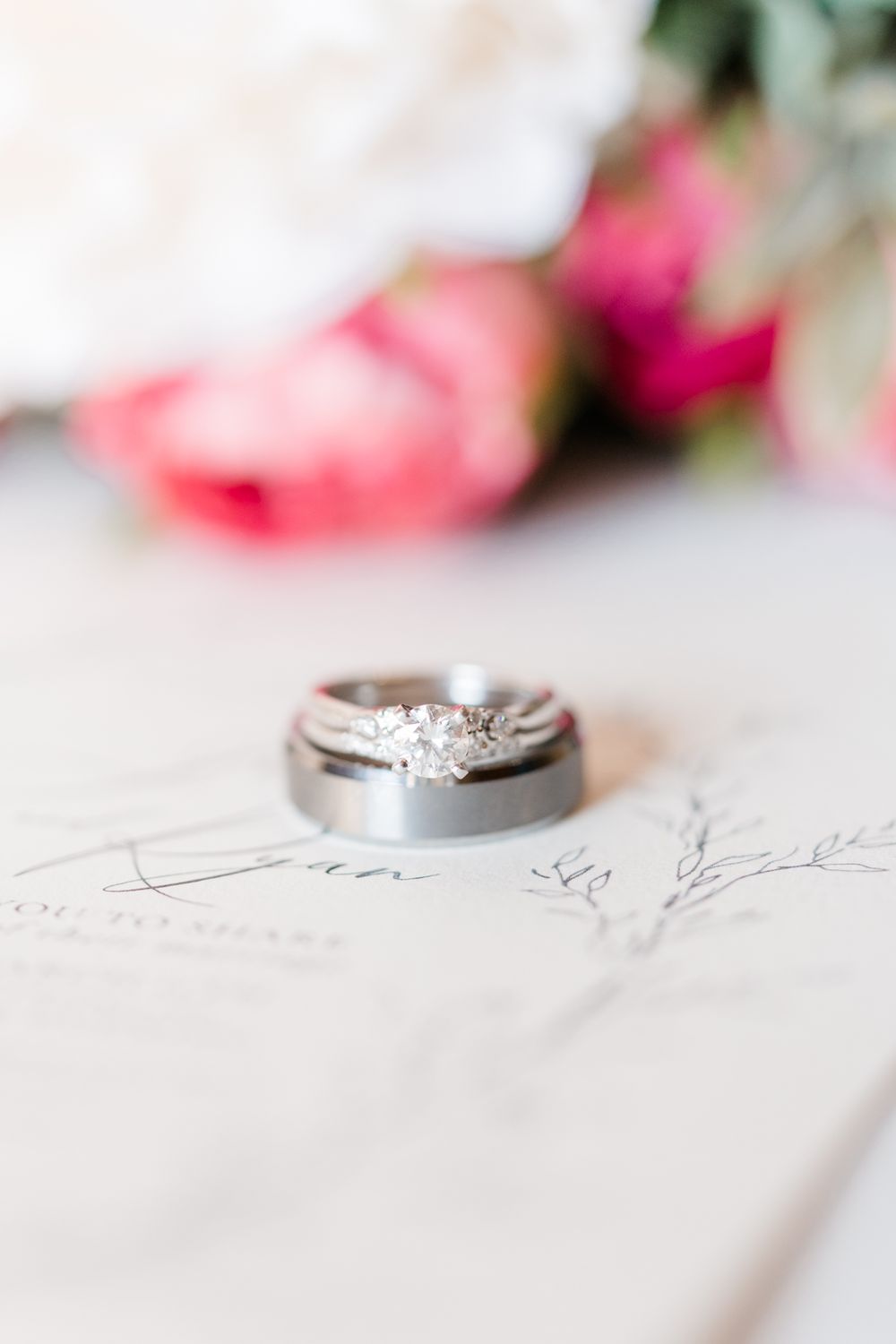 Close-up of wedding rings on paper with pink roses in the background.