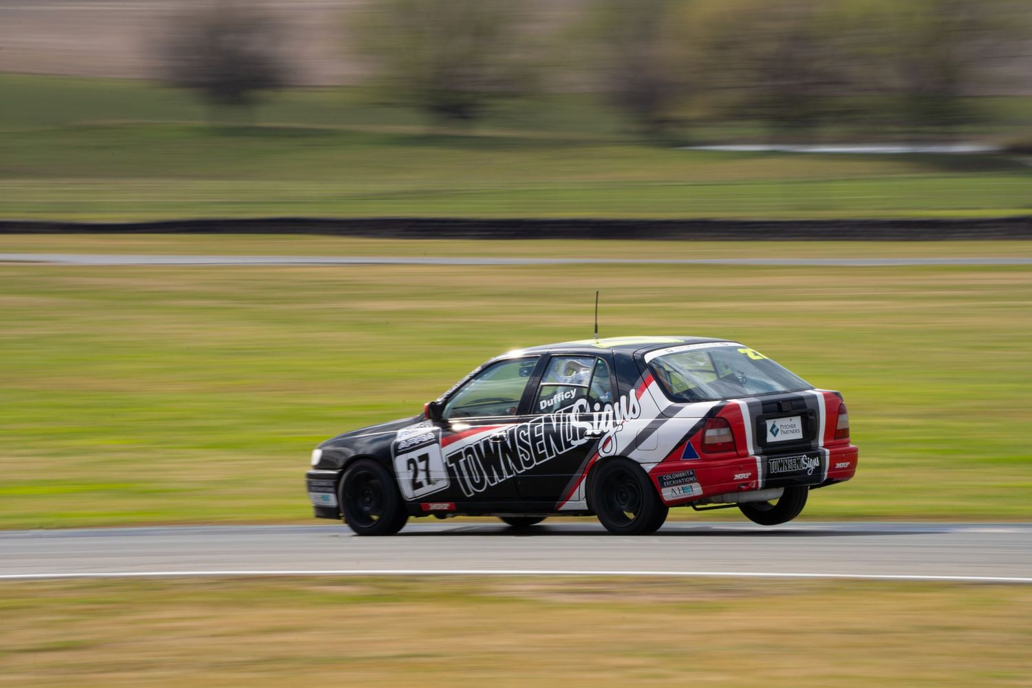 Race car with distinctive black and white livery cornering at high speed on a race track.
