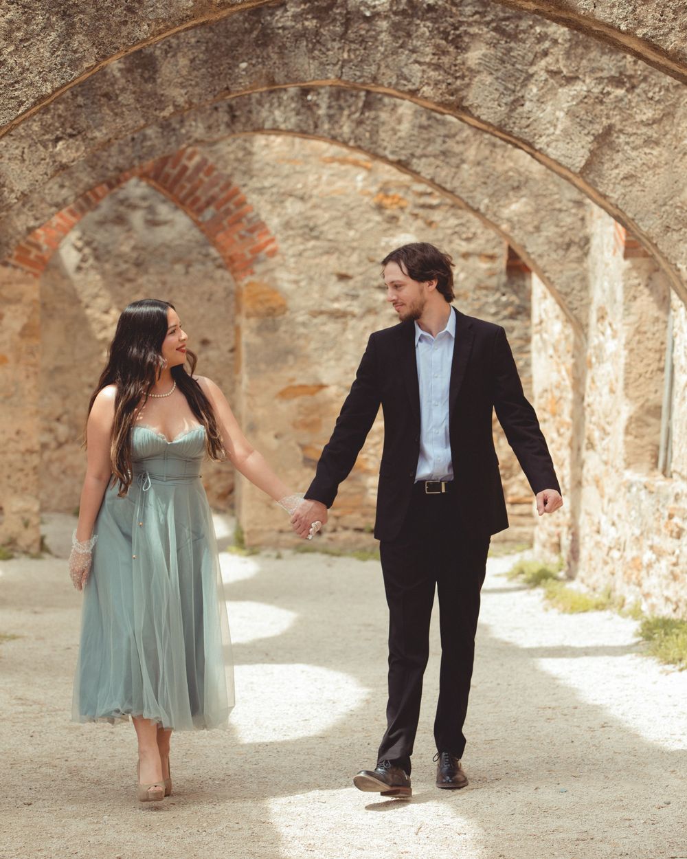 Romantic couple photoshoot under stone archways with natural lighting.