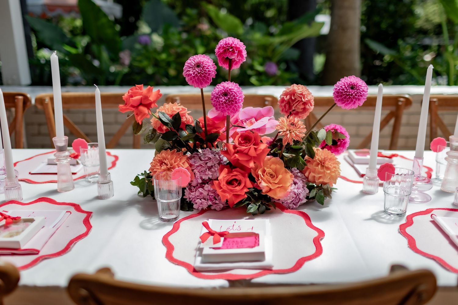 An elegant table setting with pink floral centerpieces and red-trimmed place settings.