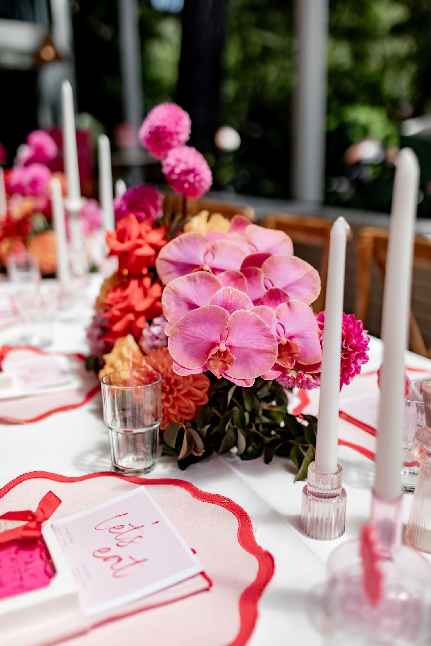 Pink orchids and vibrant floral centerpiece with white candles on an elegant table setting with red accents.