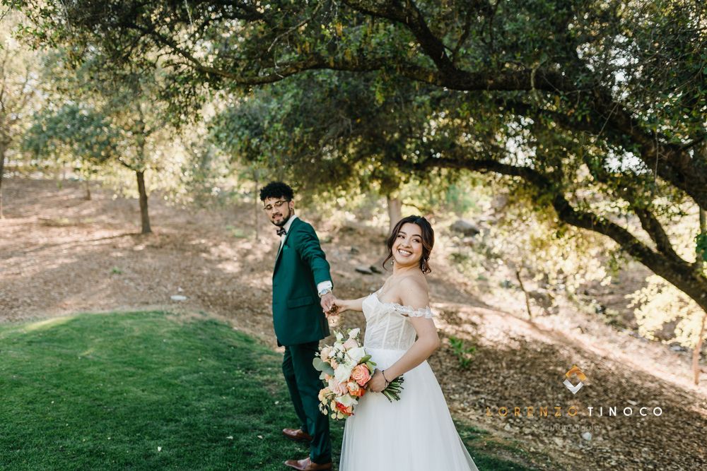 Newlyweds pose under a tree on a grassy slope during their outdoor wedding photoshoot.