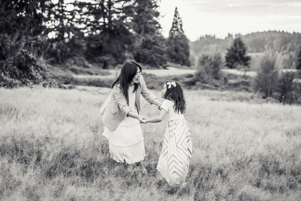 Black and white photo of mother holding hands with daughter in a field in Woodinville.