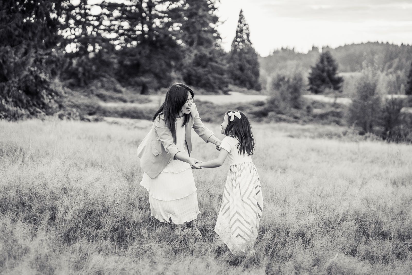 Black and white photo of mother holding hands with daughter in a field in Woodinville.