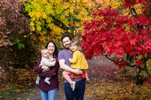Family smiling with their children in front of red and yellow fall leaves at the Seattle Arboretum.