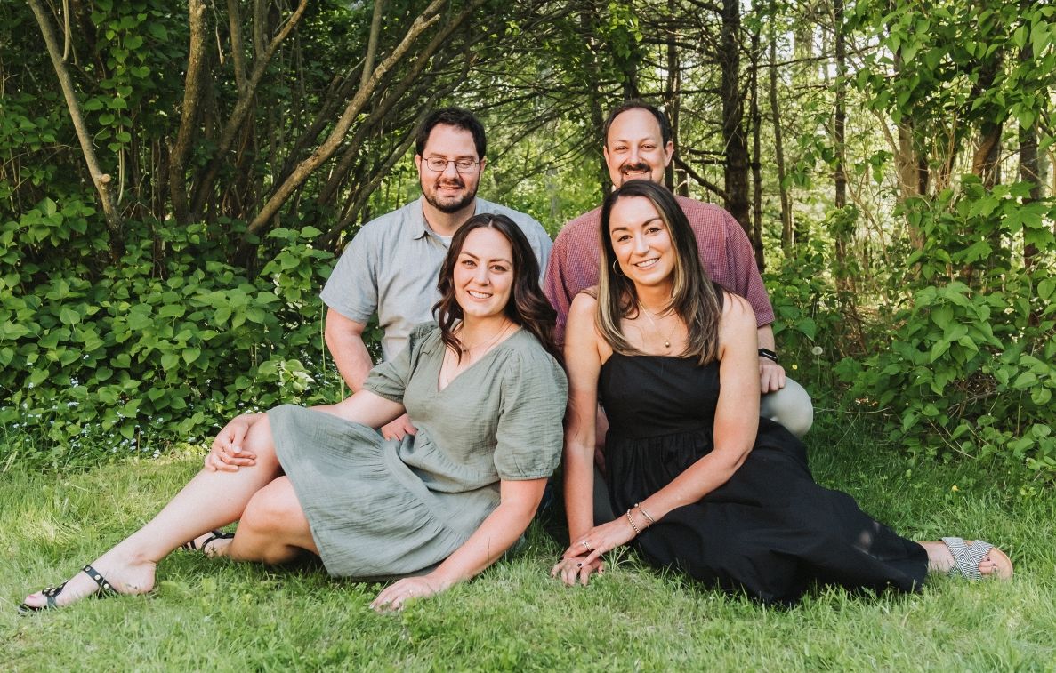 Small group relaxing together on grass in wooded outdoor setting.