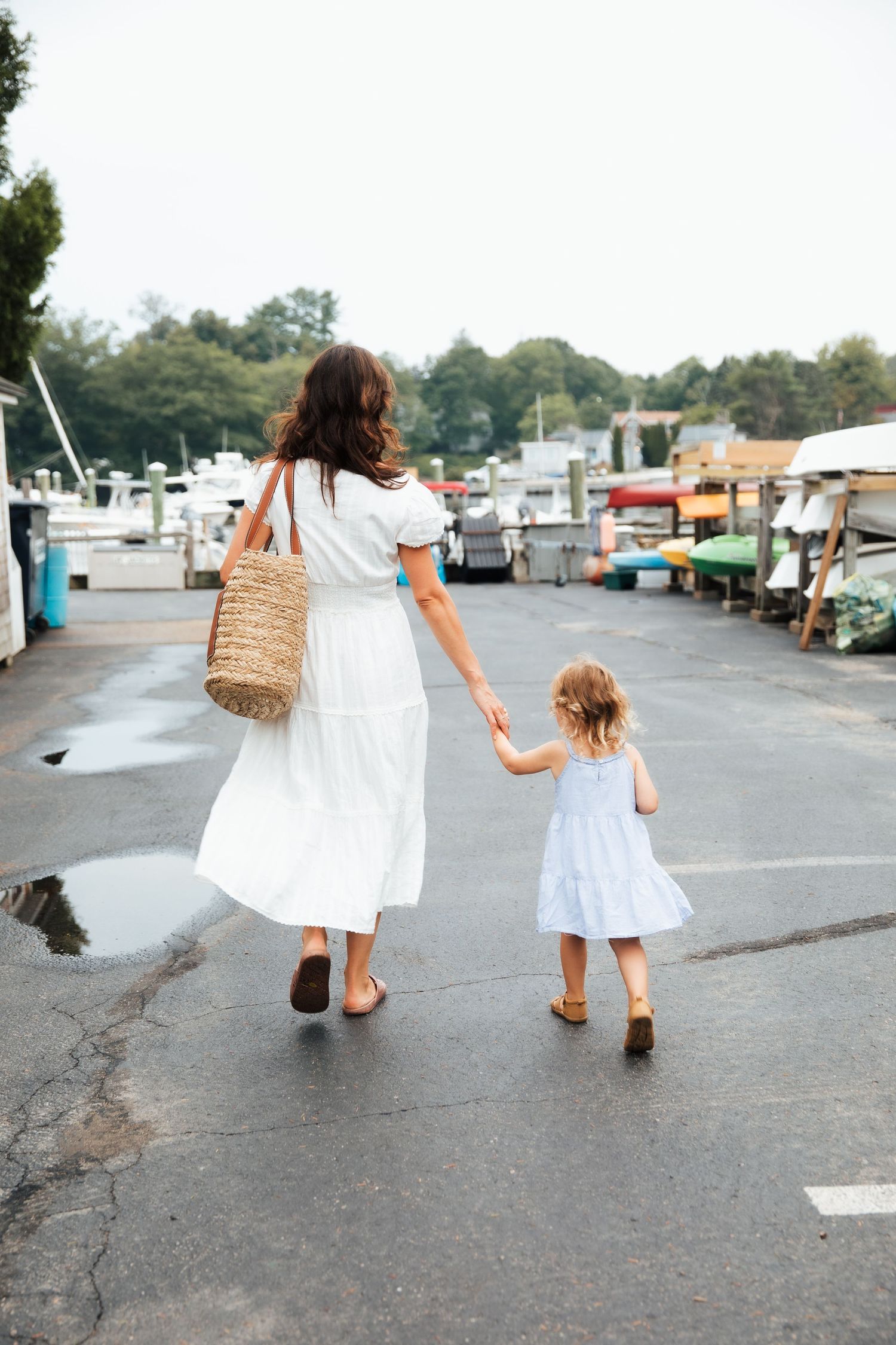 Mother and daughter in matching white dresses walking through marina holding hands.