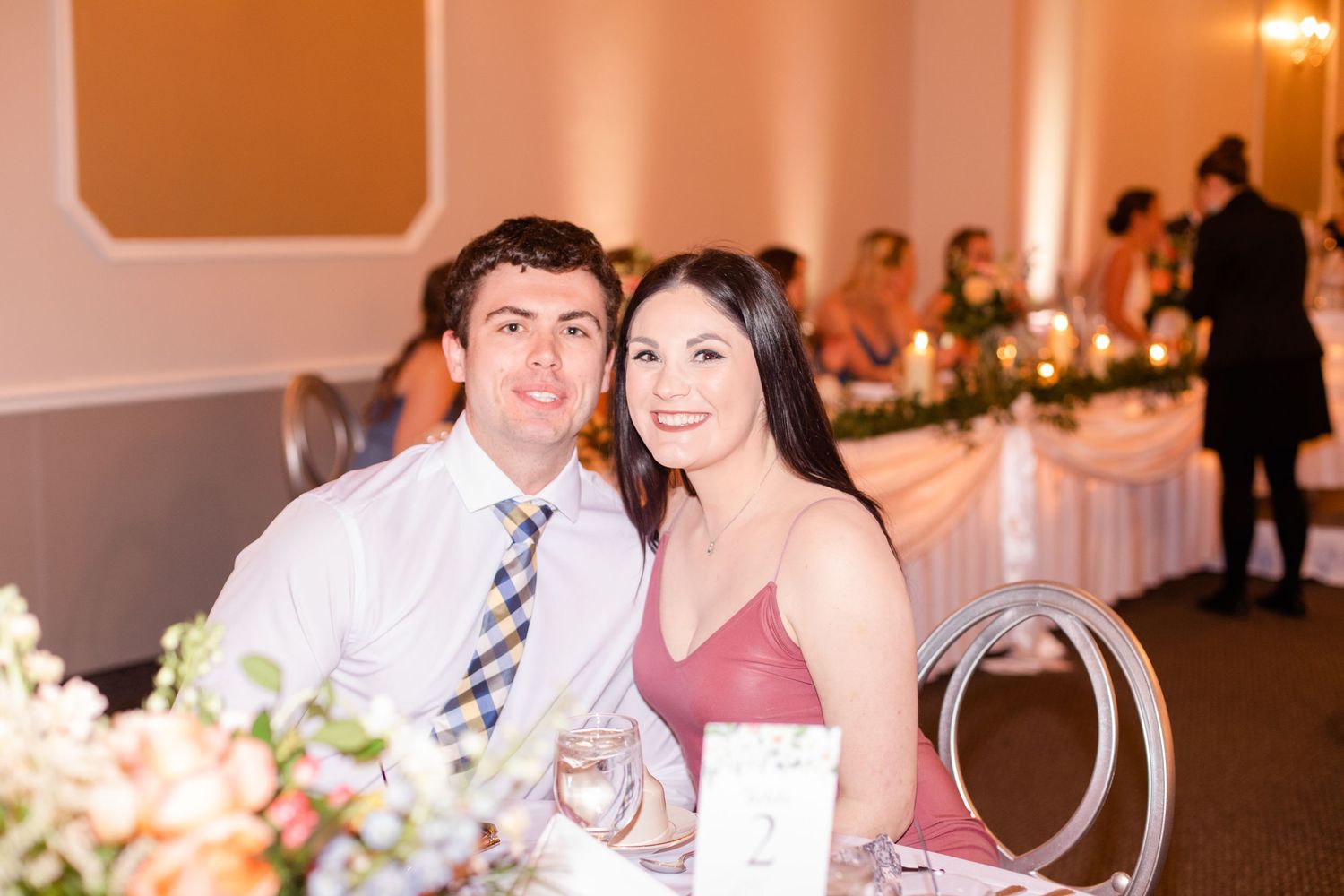Wedding reception celebration in warm-lit ballroom with decorated guest tables.