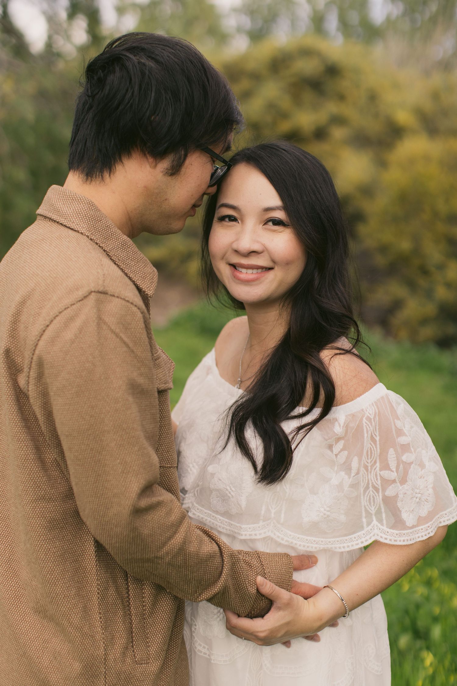 Intimate maternity photo of couple in brown and white attire against natural forest backdrop.