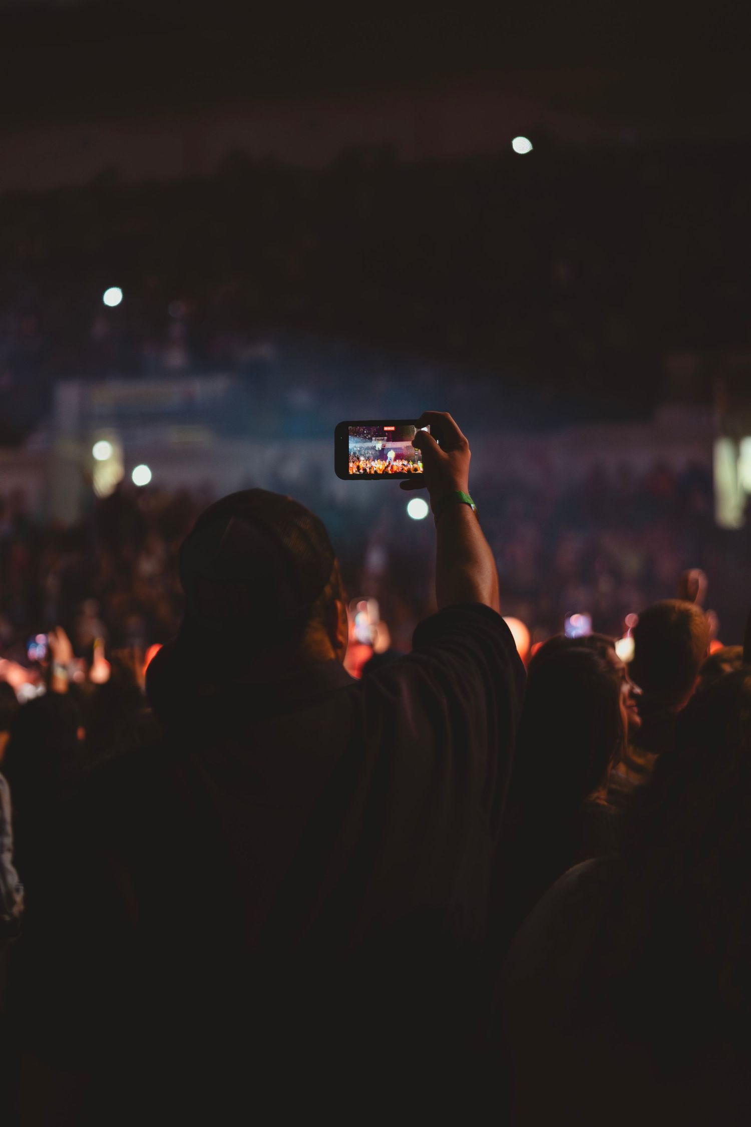 Silhouettes of concert crowd at night with phone screens glowing in darkness.