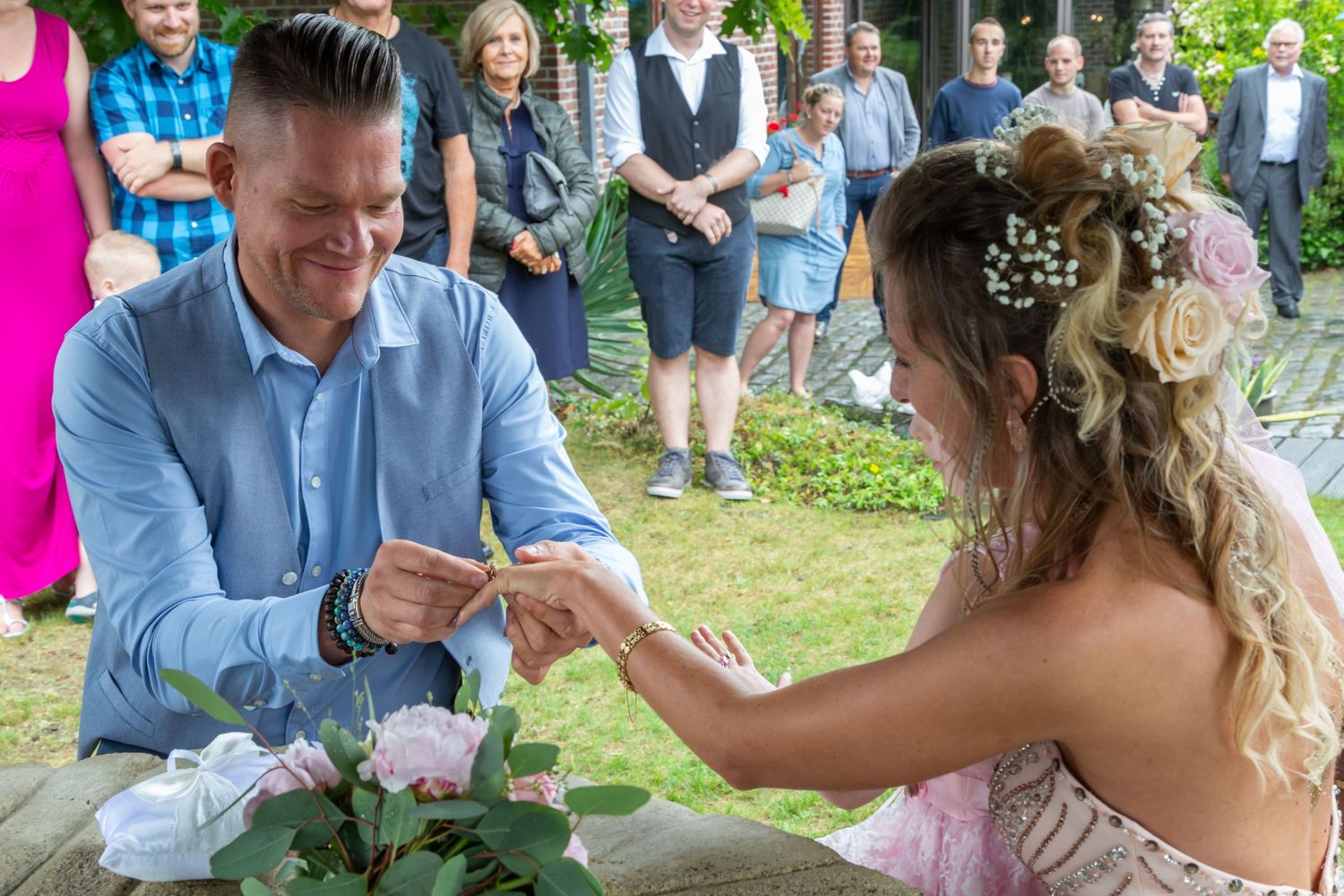 A couple exchanges rings during an outdoor wedding ceremony surrounded by guests.