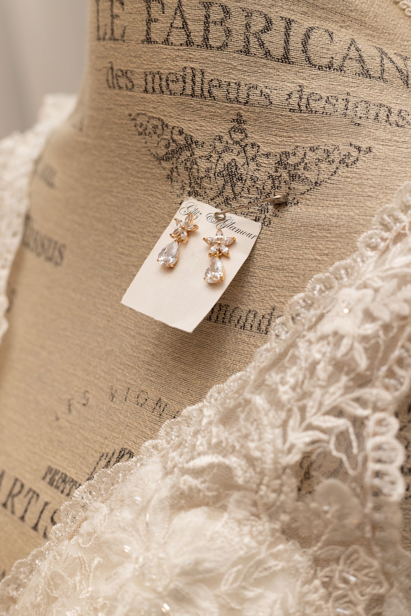 Delicate pearl earrings displayed on white card against vintage French text and lace background.