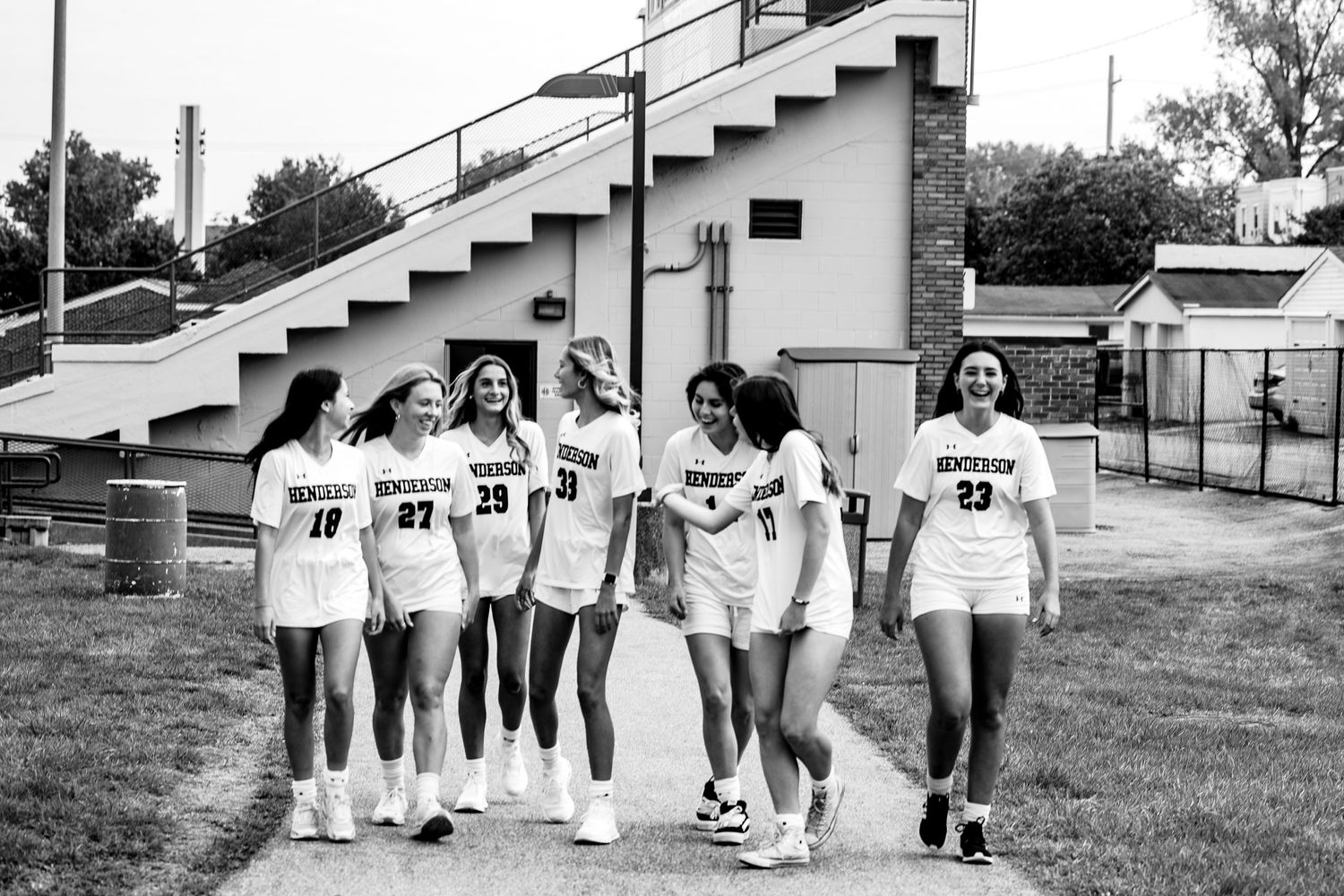 A group of athletes in matching white uniforms walking together outdoors near stadium steps.