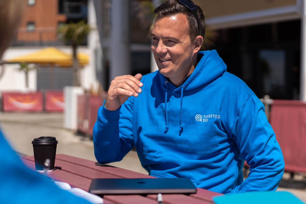 Person in bright blue hoodie sitting outdoors at table having conversation.