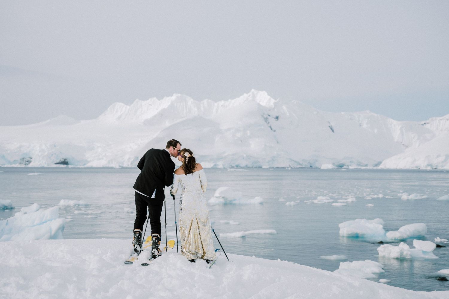 A couple on skis posing together on a snowy slope with icebergs in the background.