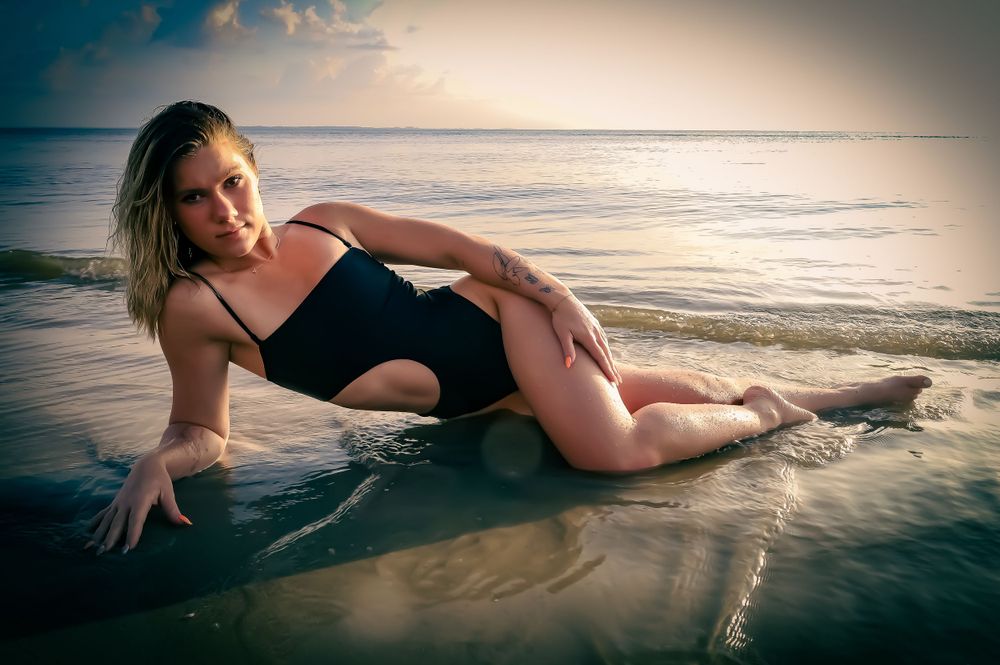 Model in red swimwear poses gracefully along the shoreline at sunset creating artistic silhouettes in the water.