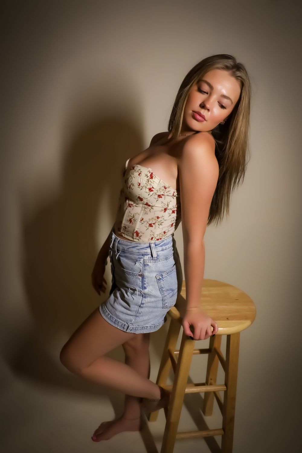 Fashion portrait with model leaning against wooden stool in casual summer attire.