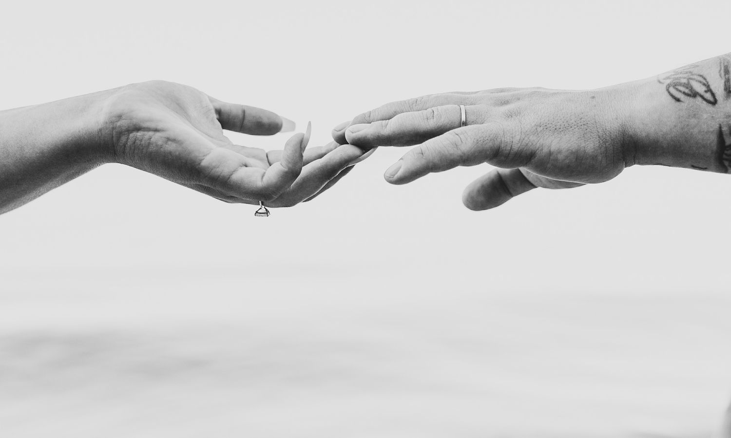 Black and white image of two hands reaching towards each other against a plain background.
