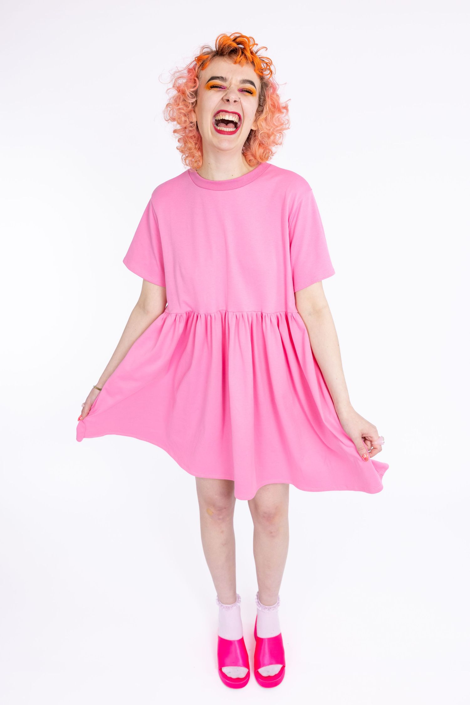 orange haired femme model wearing small business' Tallulah's Threads pink smock dress in a photography studio in Hove