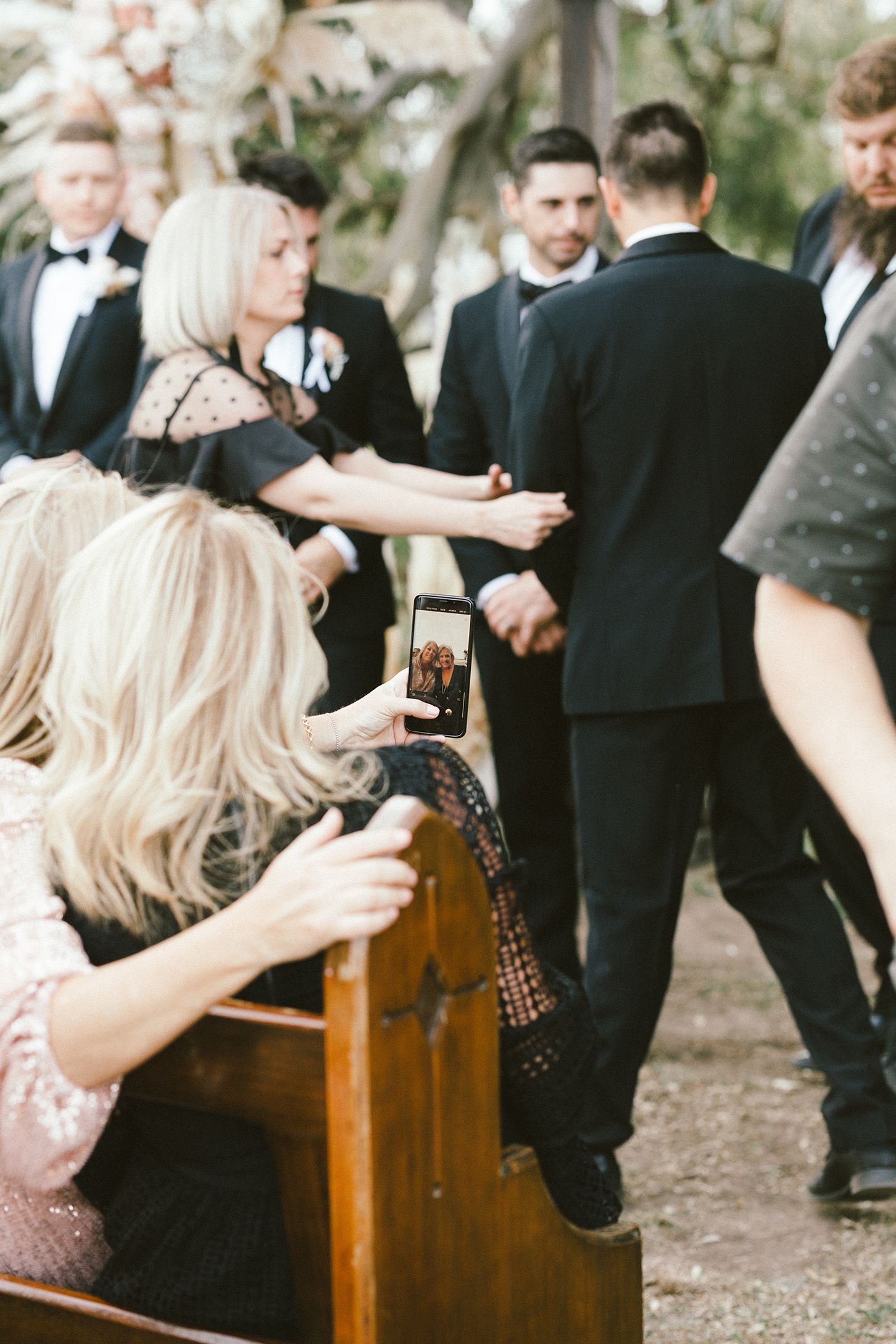 Wedding guests taking photos during formal ceremony with wooden pews.