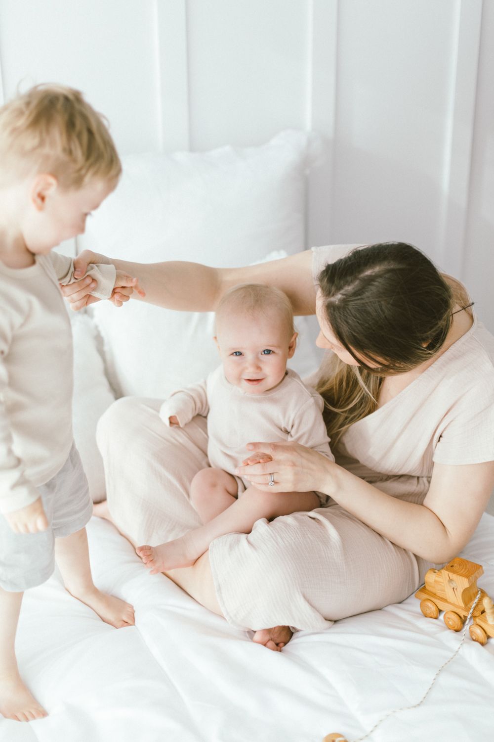 Sweet family bonding time with children on white bedding and wooden toys.