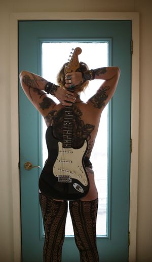 Artistic backlit portrait features electric guitar against turquoise door.