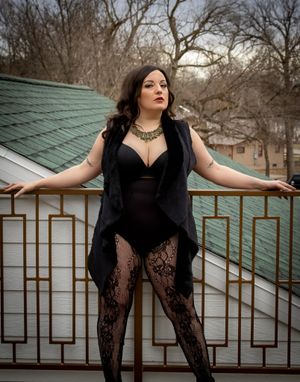 Silhouette against turquoise roof wearing black lace and vest in moody outdoor setting.