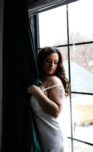 Dramatic window light portrait with teal curtains in intimate indoor setting.