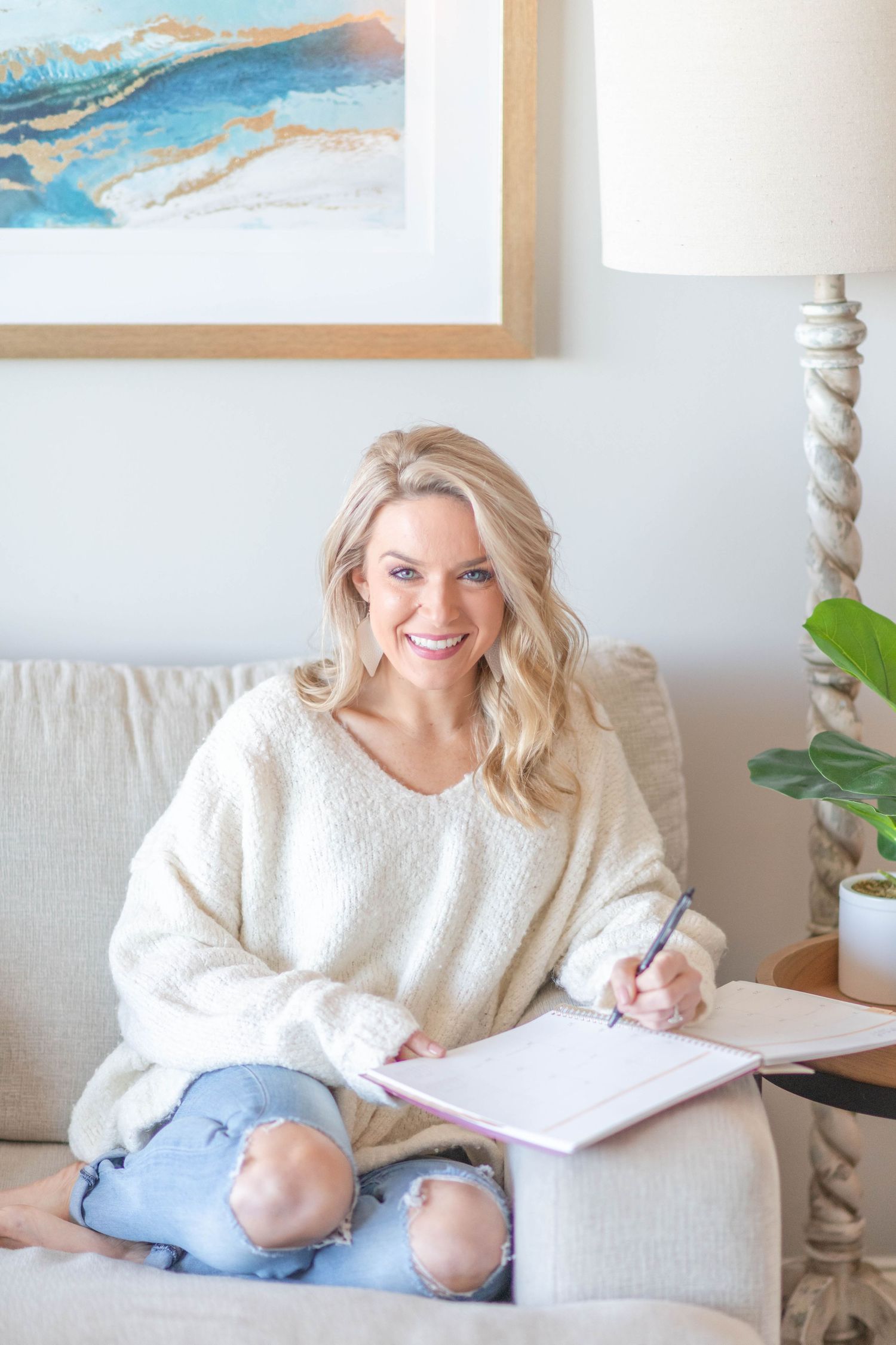Lafayette, Indiana Photographer in white sweater writing in notebook while sitting comfortably on beige couch.