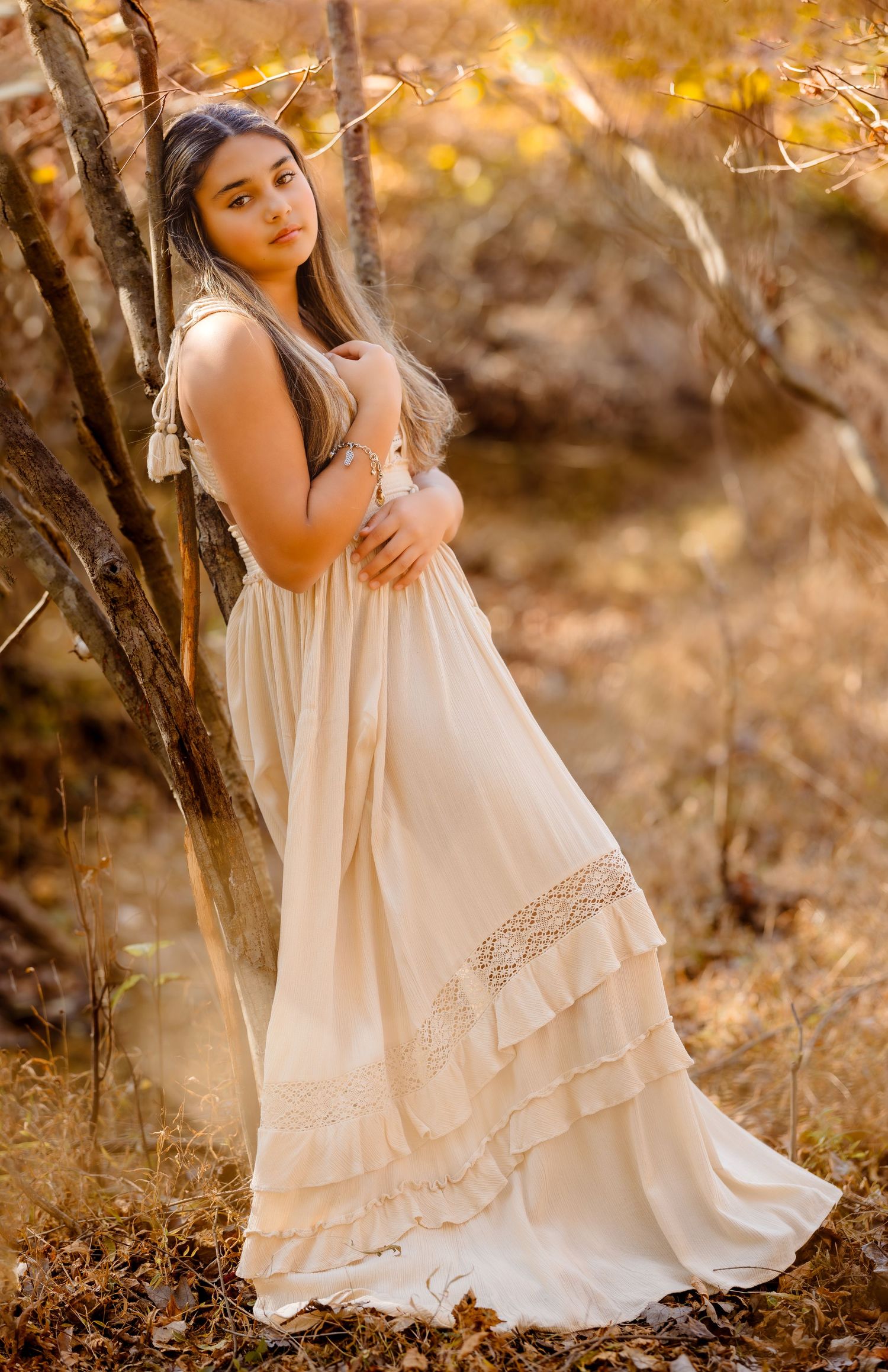 Child in vintage-style cream dress posing among autumn leaves at sunset.