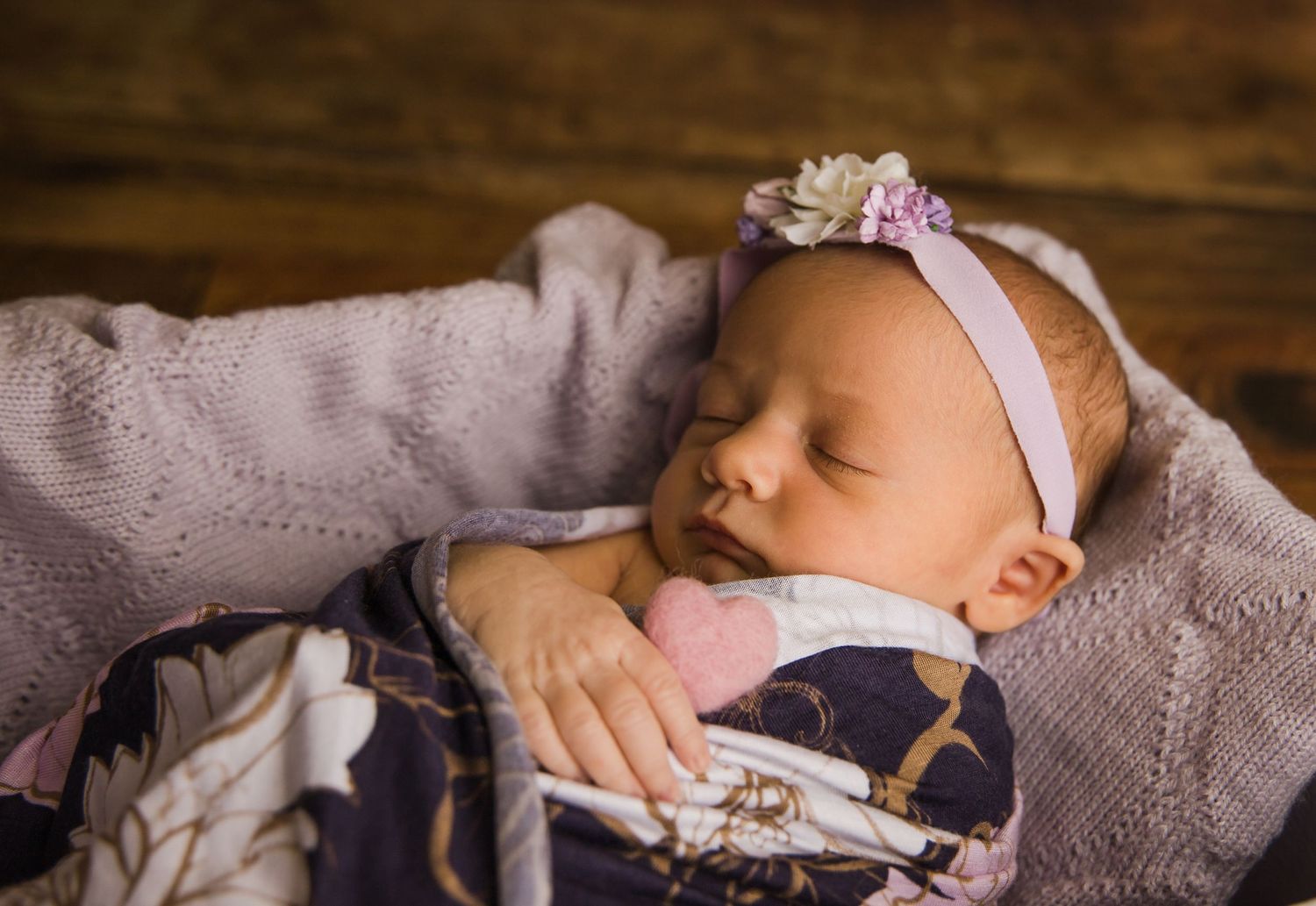 Close-up of sleeping newborn with delicate headband wrapped in navy floral swaddle.