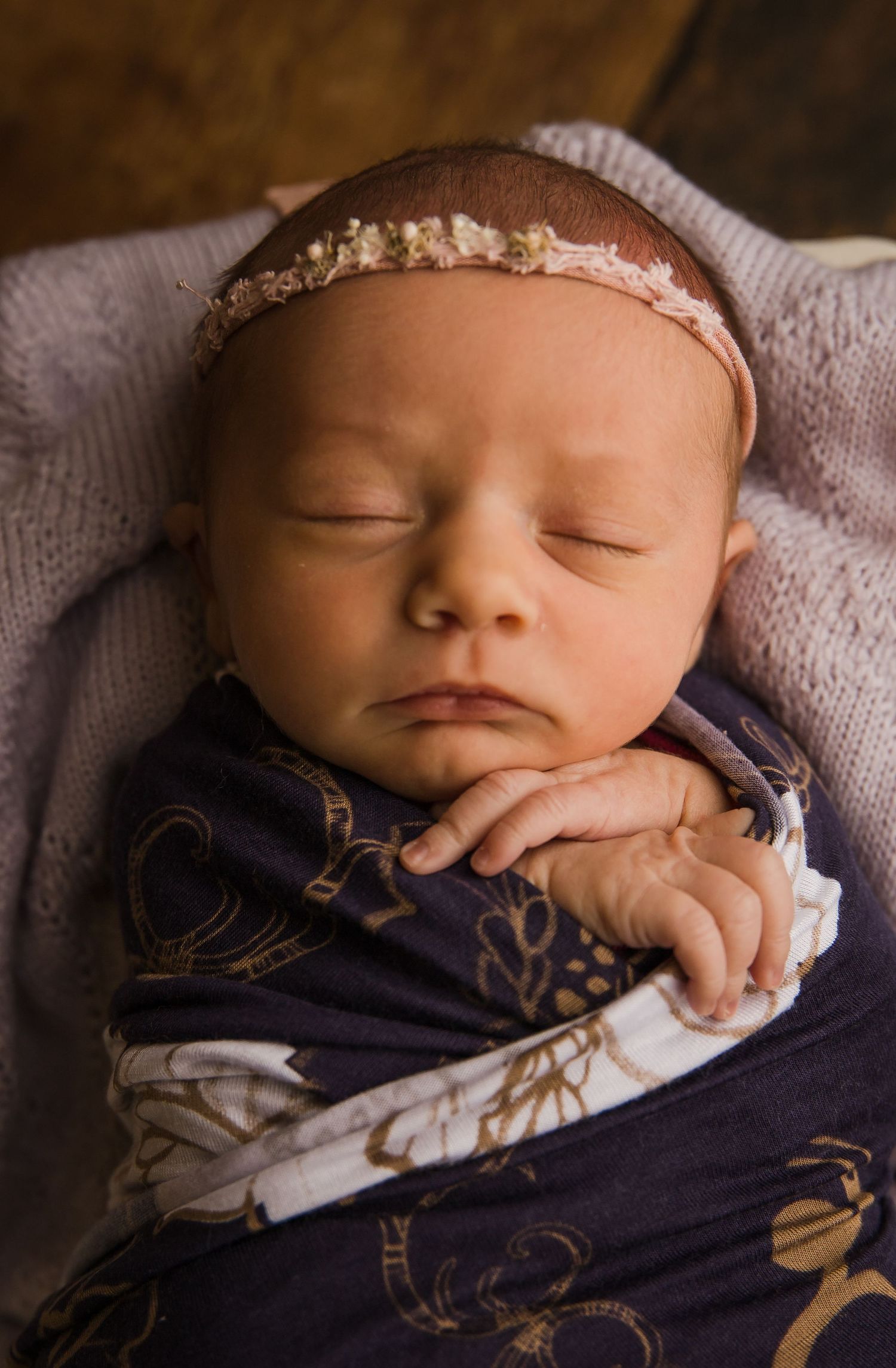 Closeup of sleeping newborn wearing delicate headband and navy floral wrap.
