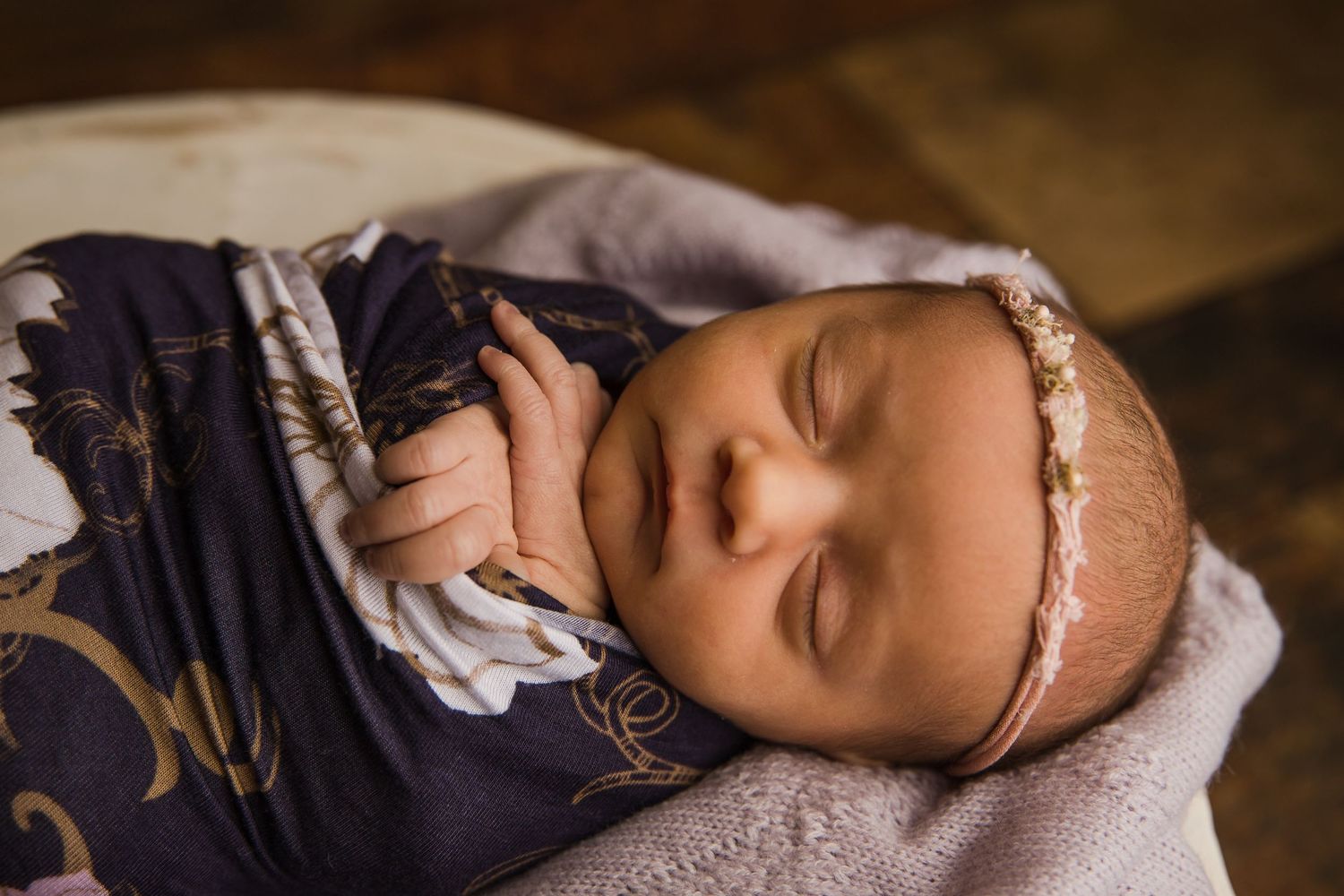 A peaceful sleeping newborn in navy outfit and lace headband on light blanket.