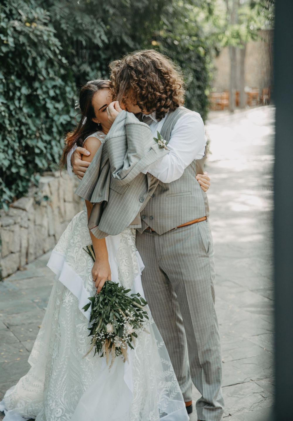 Stylish couple embracing on stone pathway with ivy-covered wall backdrop.