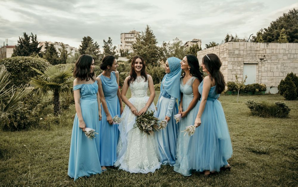 Wedding party in light blue bridesmaid dresses pose together on grassy lawn.