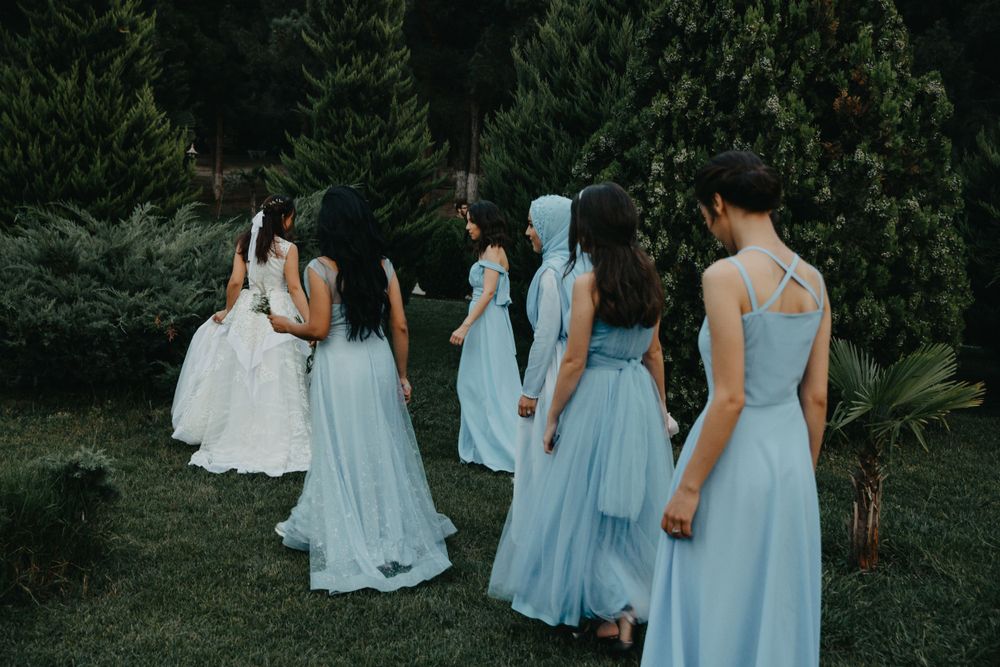 Bridesmaids in flowing light blue gowns walking through garden setting.