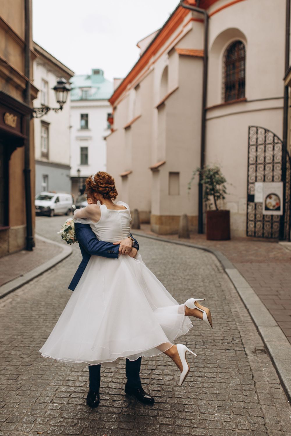A romantic dance pose on a cobblestone street with a flowing white dress and navy suit.
