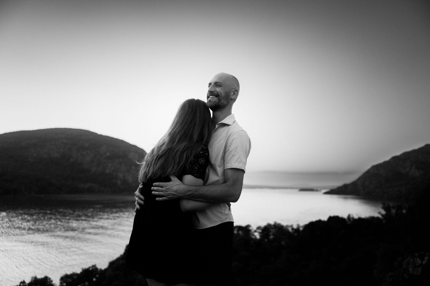 A loving couple shares an intimate moment overlooking a scenic water view at dusk.