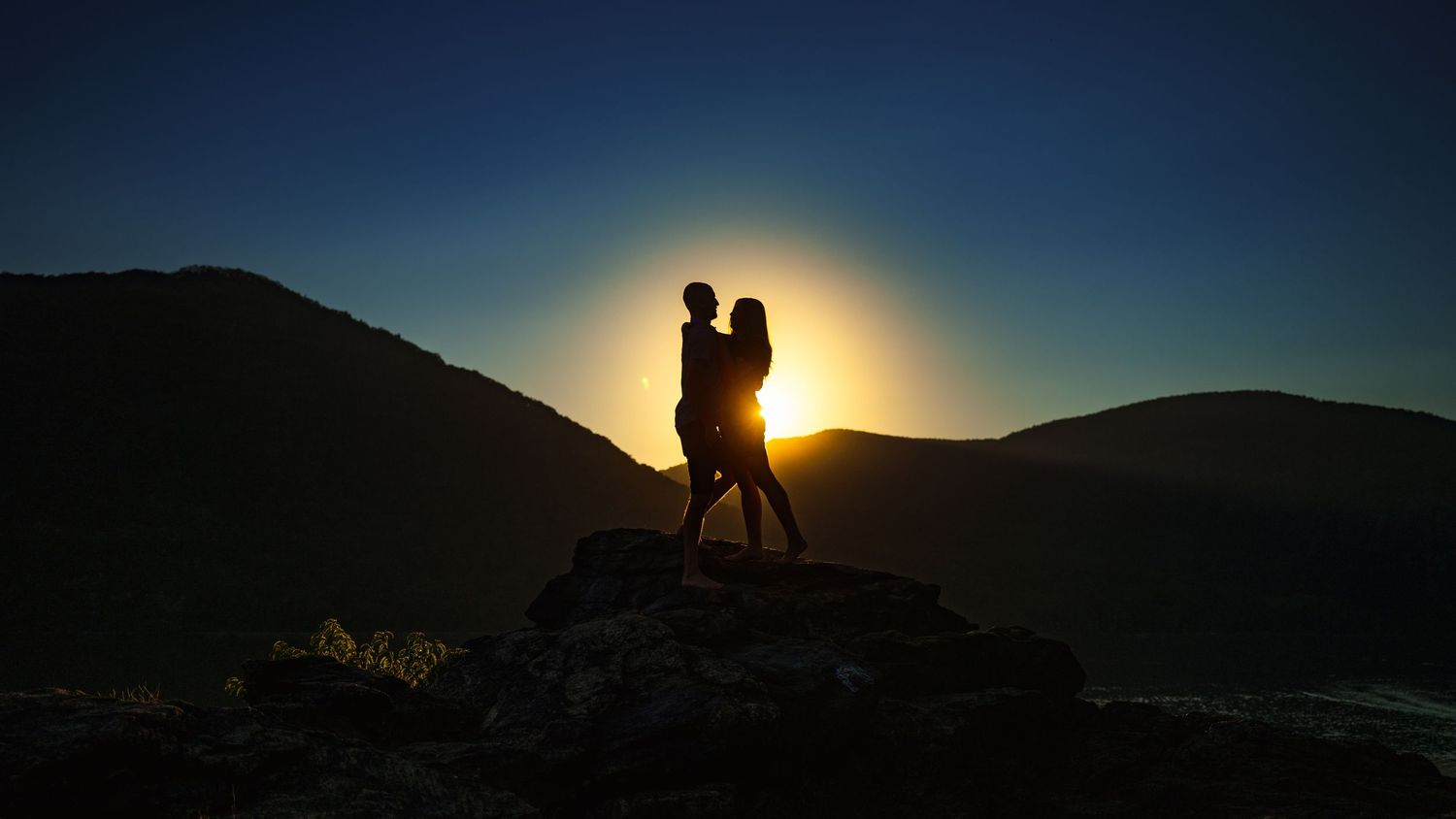 A couple's silhouette against a golden sunset on a mountain ridge.