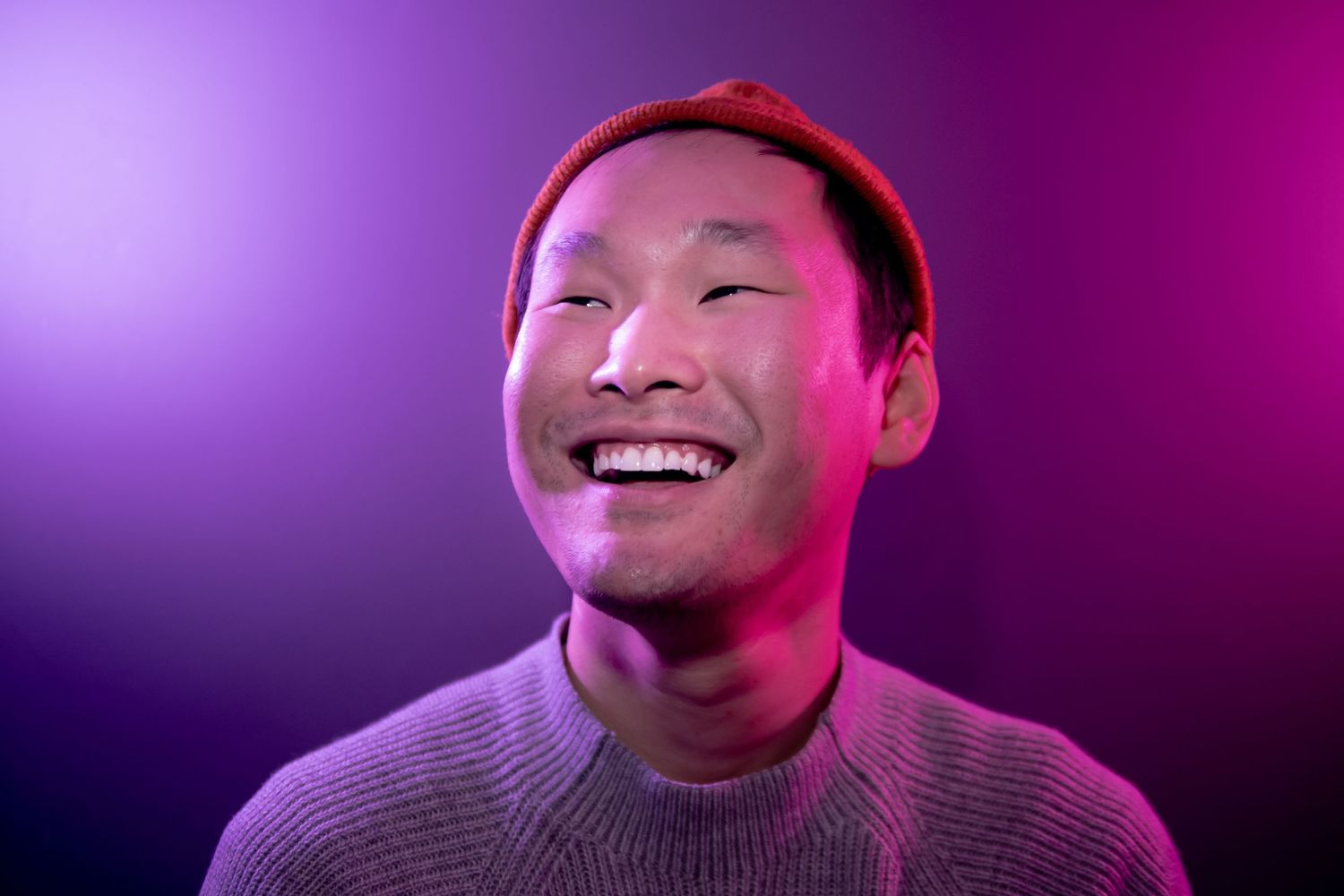 Asian Man smiling into the distance with purple and pink lights around him.