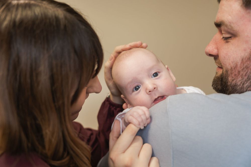 image of newborn baby looking over father's shoulder with mother stroking his head