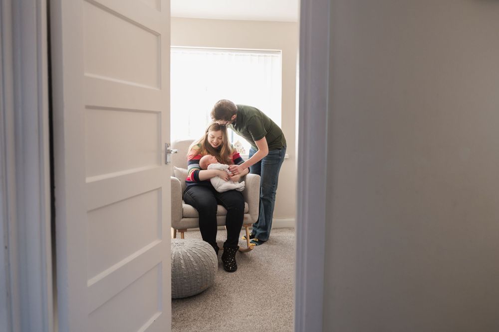 photograph of newborn baby being held by mother and father in nursery shot through door
